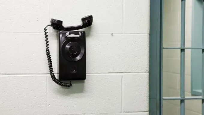 A phone hanging from a brick wall. The phone is off the hook.