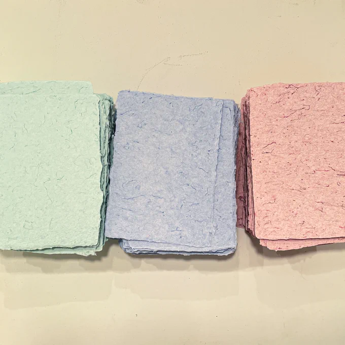 Above shot of 3 stacks of scrubs paper. There is a green stack, blue stack, and pink stack. 