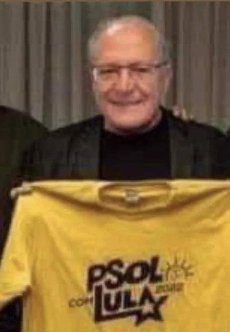 Geraldo Alckmin sorrindo segurando camiseta amarela escrito "psol com lula"