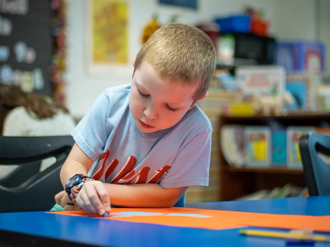 A student colors a photo using pastel crayons.