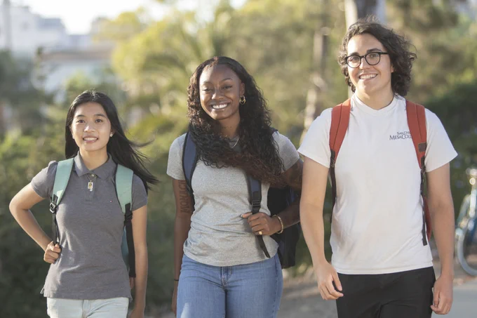 Three students wearing backpacks are walking on campus.