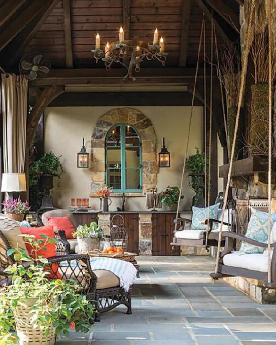 A gray tiled patio with arched ceiling features chair swings, a potted plant, and brown wicker furniture, as well as a metal light fixture.