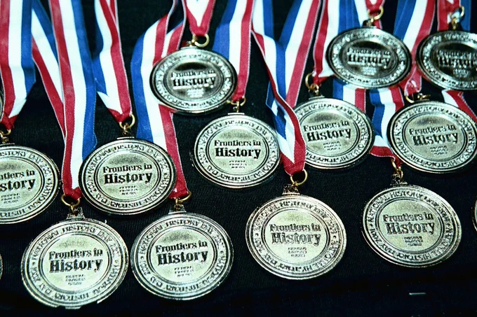 Image: Gold medals with the Frontiers in History logo laying on a table. 