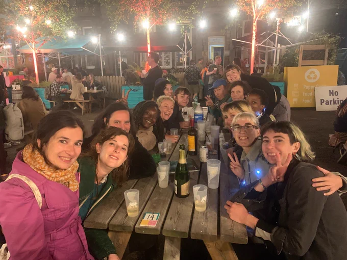 A group of artists, producers and production managers sat round a table at summerhall courtyard smiling at the camera. 