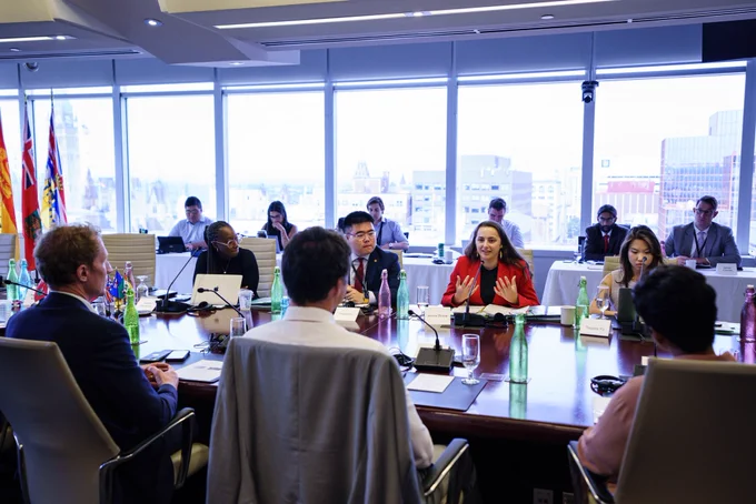 A young person, who is a member of the Prime Minister Youth Council, is sitting and speaking. They are gesturing with their hands. Others are sitting on either side of them. Prime Minister Justin Trudeau, and Ministers Marc Miller and Marci Ien, are sitting across from them.