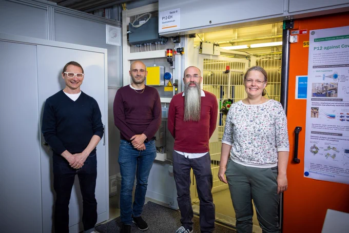 Haydyn, Clement, Cy and Melissa are standing in front of the open hutch of the P12 beamline. They are smiling and looking forward to greeting you in Hamburg.