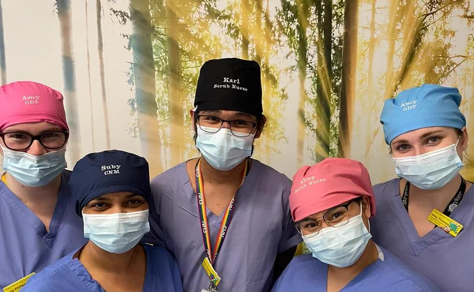 Picture showing four staff members wearing new reusable hats. They are in different colours and have the names and job roles of the staff members embroidered onto the hat.