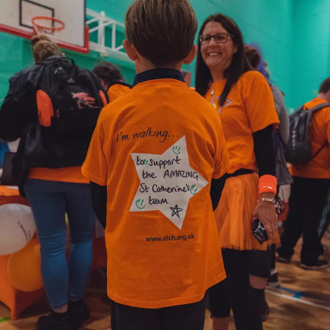 Young midnight walker wearing an orange t-shirt, facing away from the camera. The back of the t-shirt reads 'I'm Walking... to support the AMAZING St Catherine's team'.