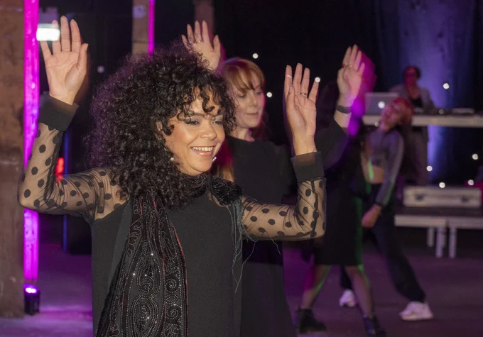 Two smiling women dance, with their hands in the air