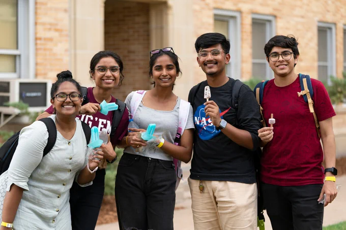 five students standing in Academic Plaza smiling, eating popsicles, and posing for a photo together.
