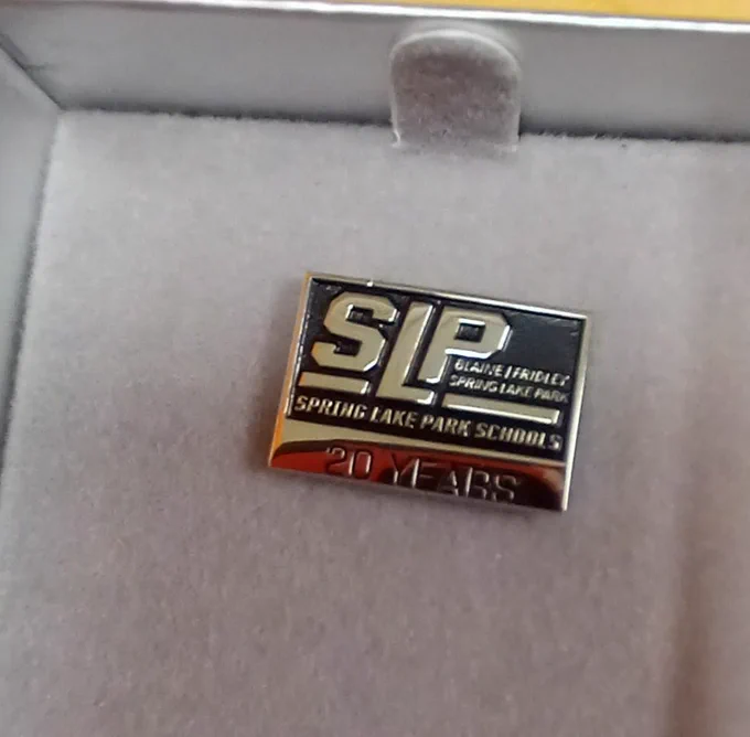 Rectangle pin, silver with black etching. Reads 'SLP. Spring Lake Park Schools. Blaine Fridley Spring Lake Park. 20 Years.'