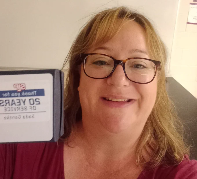 Photo of Teacher holding pin box labeled 'thank you for 20 years of service. Sada Ganske.'