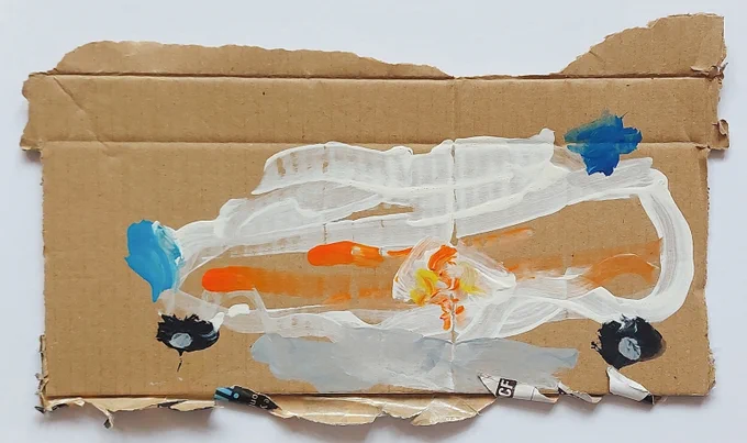 Photograph of a piece of cardboard with a truck painted on it. The vehicle is white with black wheels and two blue spots, and an orange streak runs down its side.