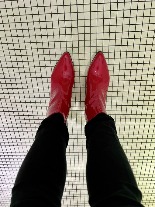 Picture taken looking down on my feet. My trousers are black skinny jeans and the shoes are a bright red pointy heeled boots in a pvc material. The floor is white tiles