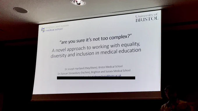 Photo of a slide projected on to a screen. Top left is the Brighton and Sussex med school logo, top right is the university of bristol. The slide reads

 “are you sure it’s not too complex?” 
- novel approach to working with equality, diversity and inclusion in medical education 
Dr Joseph Harland (they/them) 
Dr Duncan Shrewsbury (he/him)