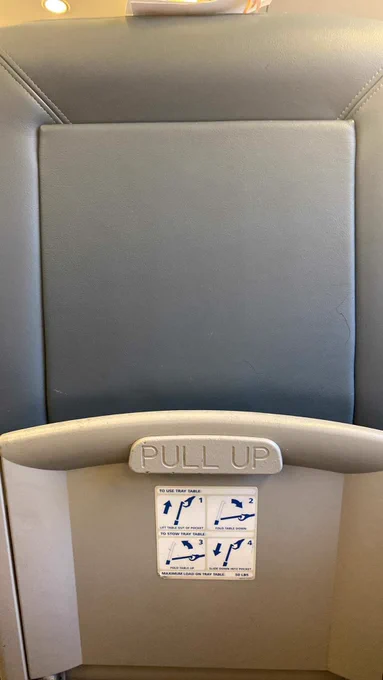 Picture depicts an inadvertently aggressive tan sign on the back of a gray Amtrak seat that reads “Pull Up,” a phrase commonly associated with initiating a fight.