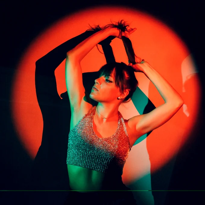Erin Kilmurray highlighted in a red spotlight, ponytail in hand & posed