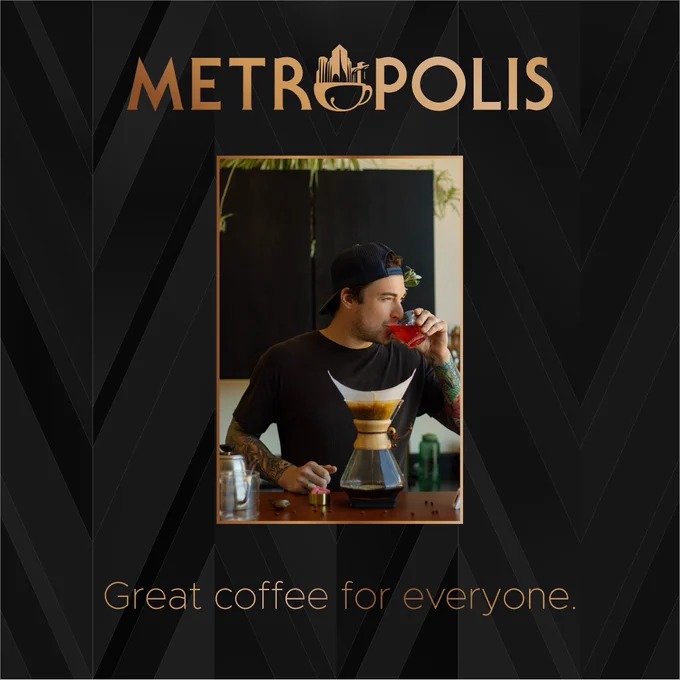 One of the Roasters at Metropolis drinks a glass of fruit punch in front of a freshly brewed Chemex of Costa Rica Perla Negra. He has fresh sage tucked behind his ear, and a measuring cup of bubble gum beside him. Above the photo the Metropolis font and logo appear in a gold gradient. The background is a black gradient pattern, with the phrase “Great coffee for everyone” also written in a gold gradient.