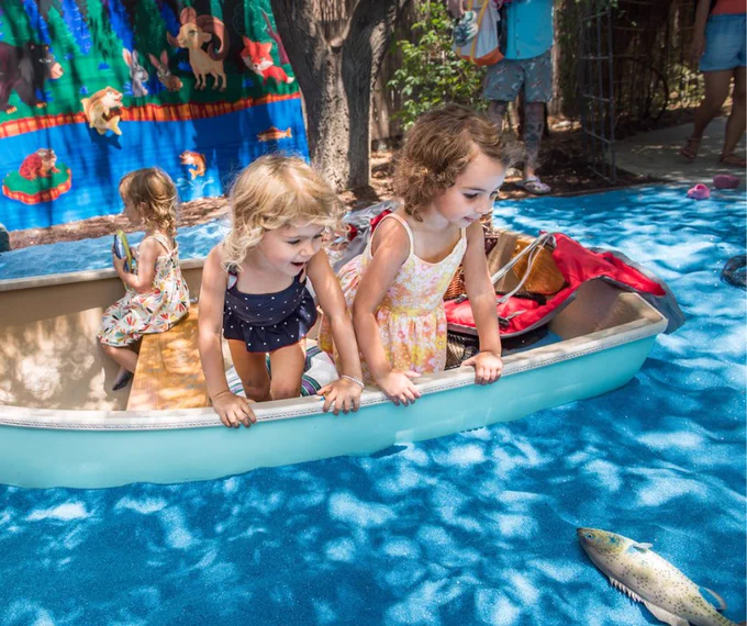 Children in a boat on blue sand looking at a pretend fish