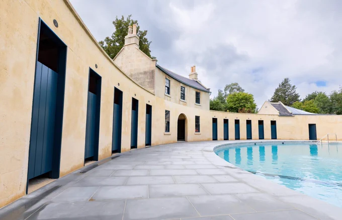 A crescent building with 12 blue doors with an outdoor swimming pool in front