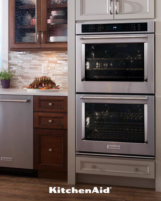 KitchenAid Double Wall Oven can be seen in the kitchen. There's a KitchenAid dishwasher to its left and a platter of evenly baked meat on the countertop.