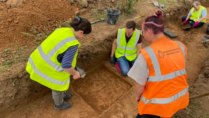 Two volunteer excavating a ditch slot under the guidance of an archaeologist