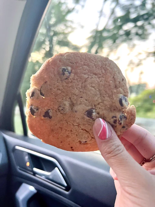 A perfectly baked soft chocolate chip cookie held in front of the setting sun in a car.
