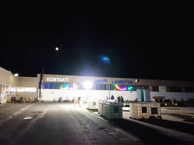 Das Kontakt Gebäude in Bamberg bei Nacht, es sind einige Menschen vor der Tür, hinter den Fenstern sieht man RGB Lichter, außen ist ein Baulicht aufgestellt das den Platz erleuchtet auf dem Gebäude steht in großen blauen Lettern "Mehr Lametta"