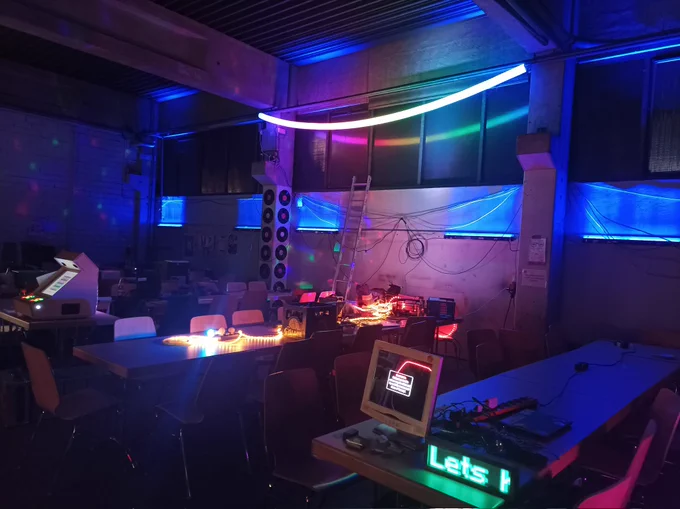 Innenansicht des Hackcenter, man sieht bunte Lichter und vereinzelt Bildschirme und eine Arcade Maschine