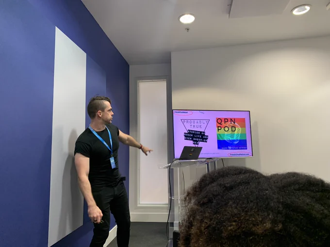 Scott’s talk on scripting for presenting. Scott is stood beside a screen. The screen has the logos of the QPN podcast and probably true. Scott is pointing at them