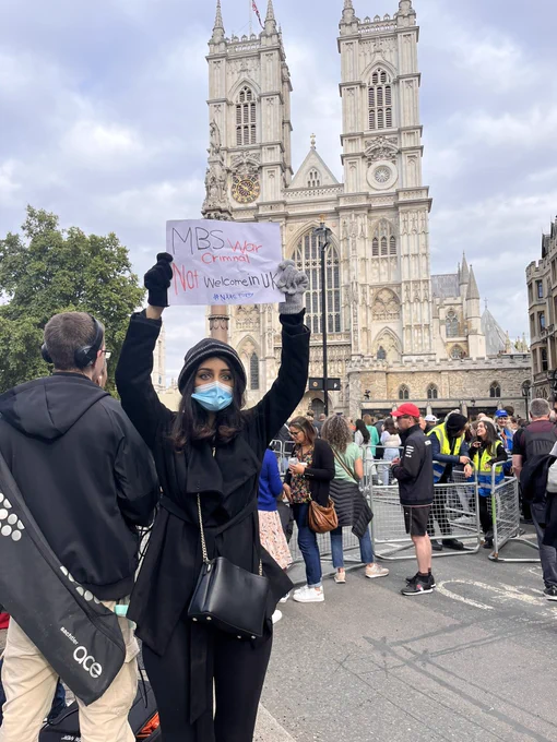A woman stands outside Westminster Abbey, where Queen Elizabeth’s funeral is to take place Monday, with a sign that says MBS War Criminal Not Welcome In U.K.