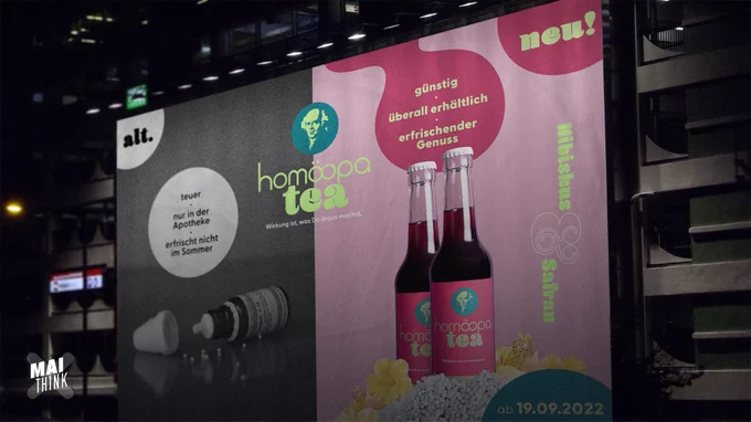 Werbeplakat, die linke Hälfte in schwarz weiß, darauf eine Globuliflasche und die Aufschrift "teuer, nur in der Apotheke, erfrischt nicht im Sommer". Rechts farbig, darauf eine HomöopaTea Flasche und die Aufschrift "günstig, überall erhältlich, erfrischender Genuss". 