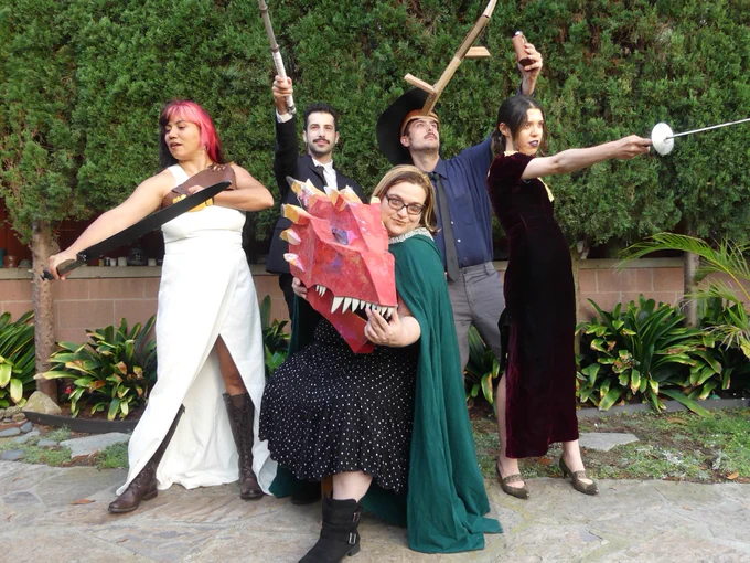 five people in suits and dresses, holding weapons and a paper mache dragon head