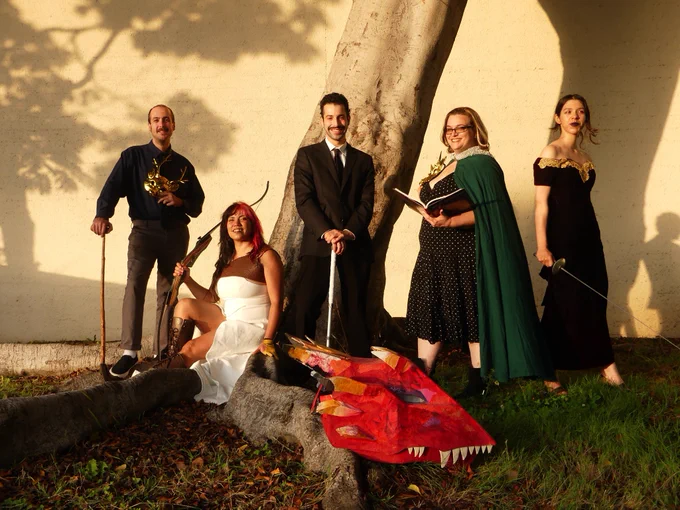 five people in suits and dresses, holding weapons and a paper mache dragon head