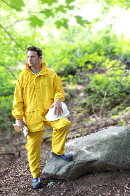 A worker wearing rain gear, holding a hard hat and work gloves
