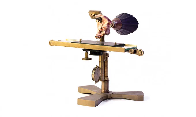 Ear phonautograph reconstruction photographed against a white background. Instrument is predominantly made of brass, with a cone-shaped black rubber mouthpiece.