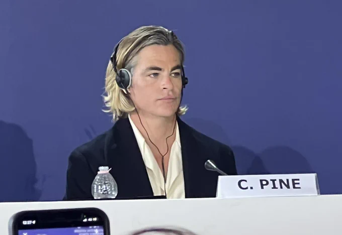 Chris Pine at the conference for Don’t Worry Darling. His face is blank and expressionless, and he wears headphones.