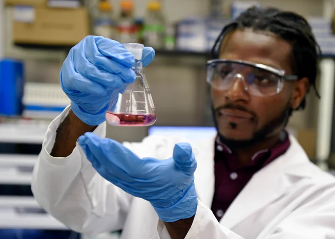 Scientist in lab coat holds beaker.