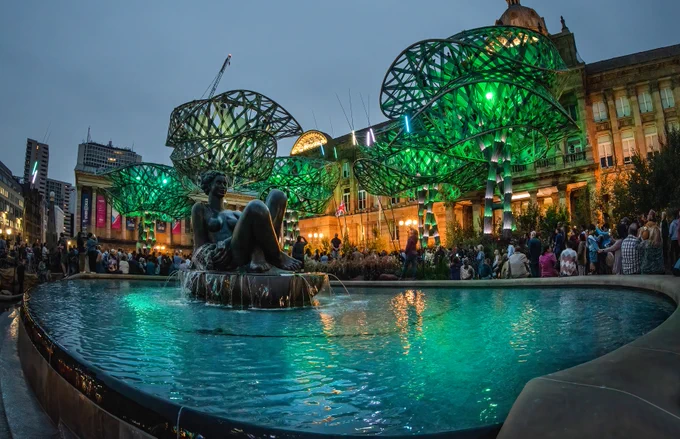 The fountain at Victoria Square and the PoliNations garden is lit up in greens while visitors look up at the lights in delight.