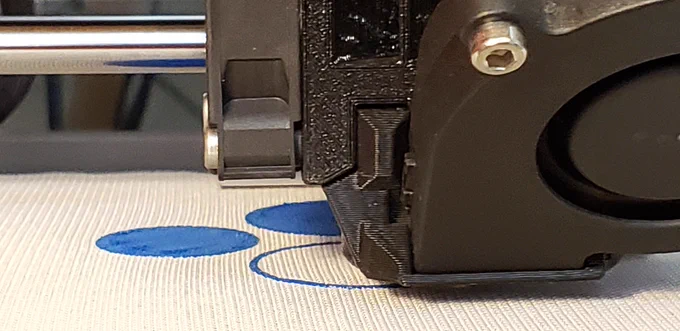 Close up of 3d printer head extruding blue plastic onto a textile surface previously printed blue circles are also visible