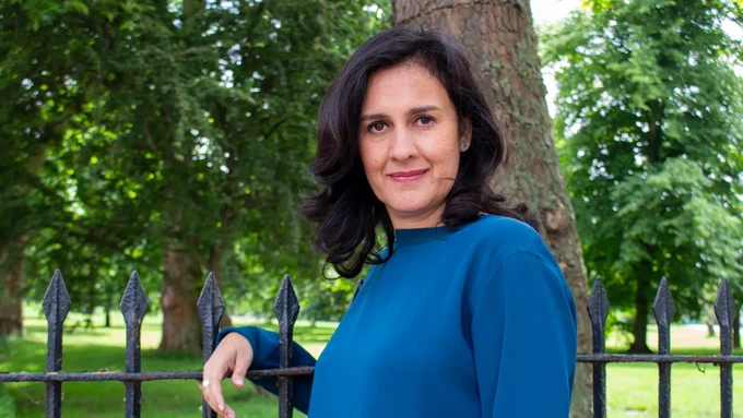 Portrait of Kamila Shamsie, leaning on a metal gate 
