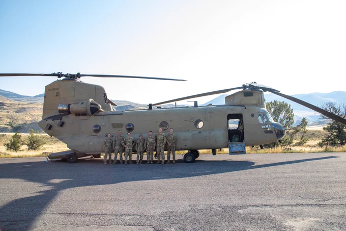 a group of seven people in military uniform standing in front of a large helicopter and smiling at the camera