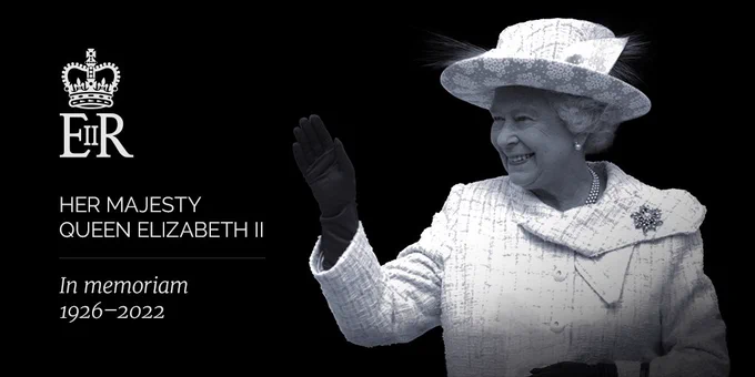 A black and white photo of Her Majesty The Queen. She is waving and smiling. Her monogram is in the top left corner of the image. White text under the monogram reads, “Her Majesty Queen Elizabeth II, In memoriam, 1926-2022.”