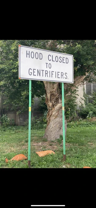 A white street sign that reads, "HOOD CLOSED TO GENTRIFIER."