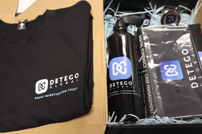 A box containing a Detego Global shirt, water bottle, display wipe, and challenge coin.