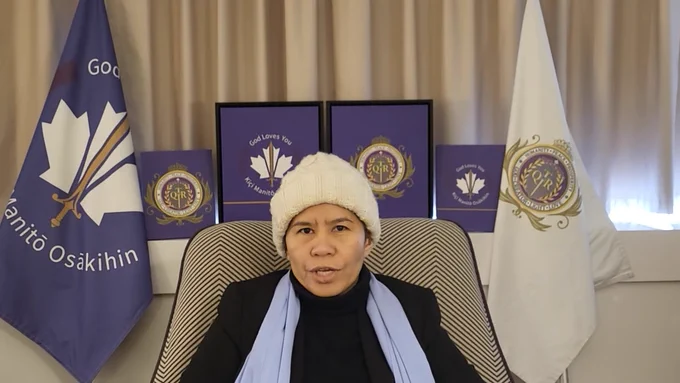 Self-proclaimed “Queen of Canada ” Romana Didulo delivers remarks virtually. She sits in front of various purple emblems with royal themes.