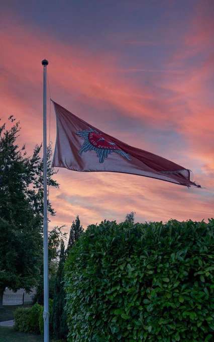 A HFRS flag is lowered to half mast against a sunset sky