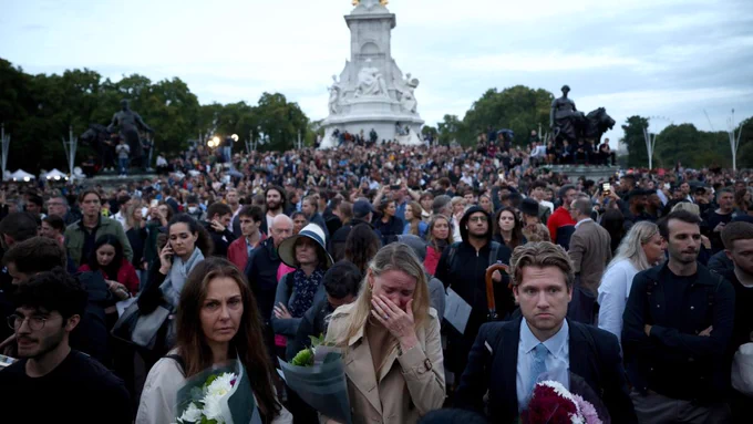 crowds in front of Bucking Palace holding flowers, a lady is crying