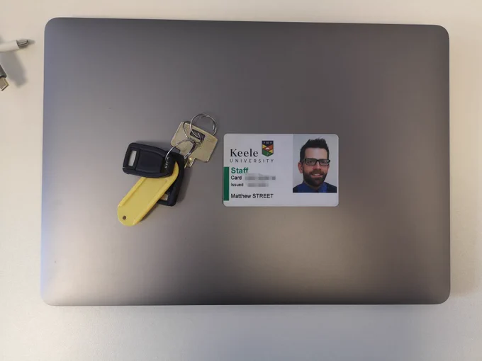 Silver laptop closed with set of keys on top and a staff identification card next to them.