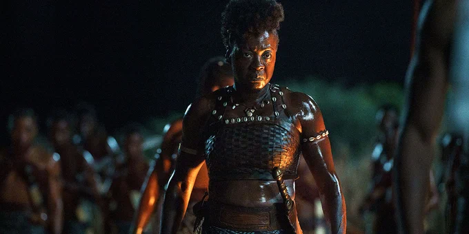 Viola Davis wearing armour, in focus with an army behind her in the background, in a still frame from the film The Woman King.